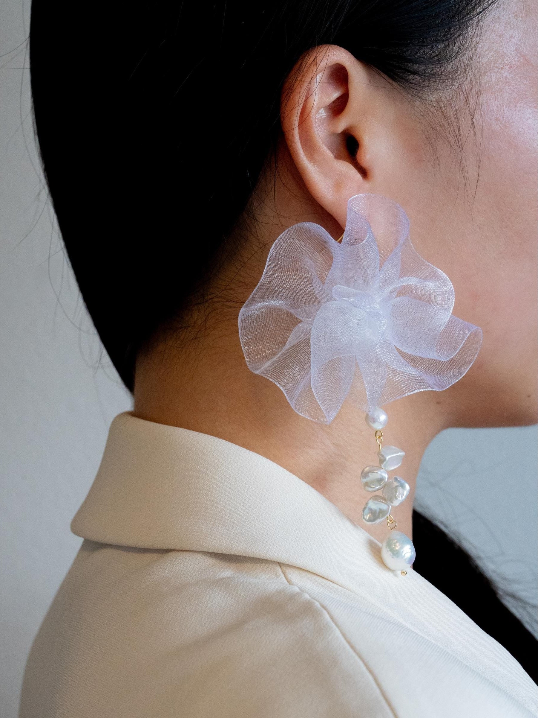 Close-up of a person wearing a white organza floral earring with natural freshwater pearls drop in a neutral background