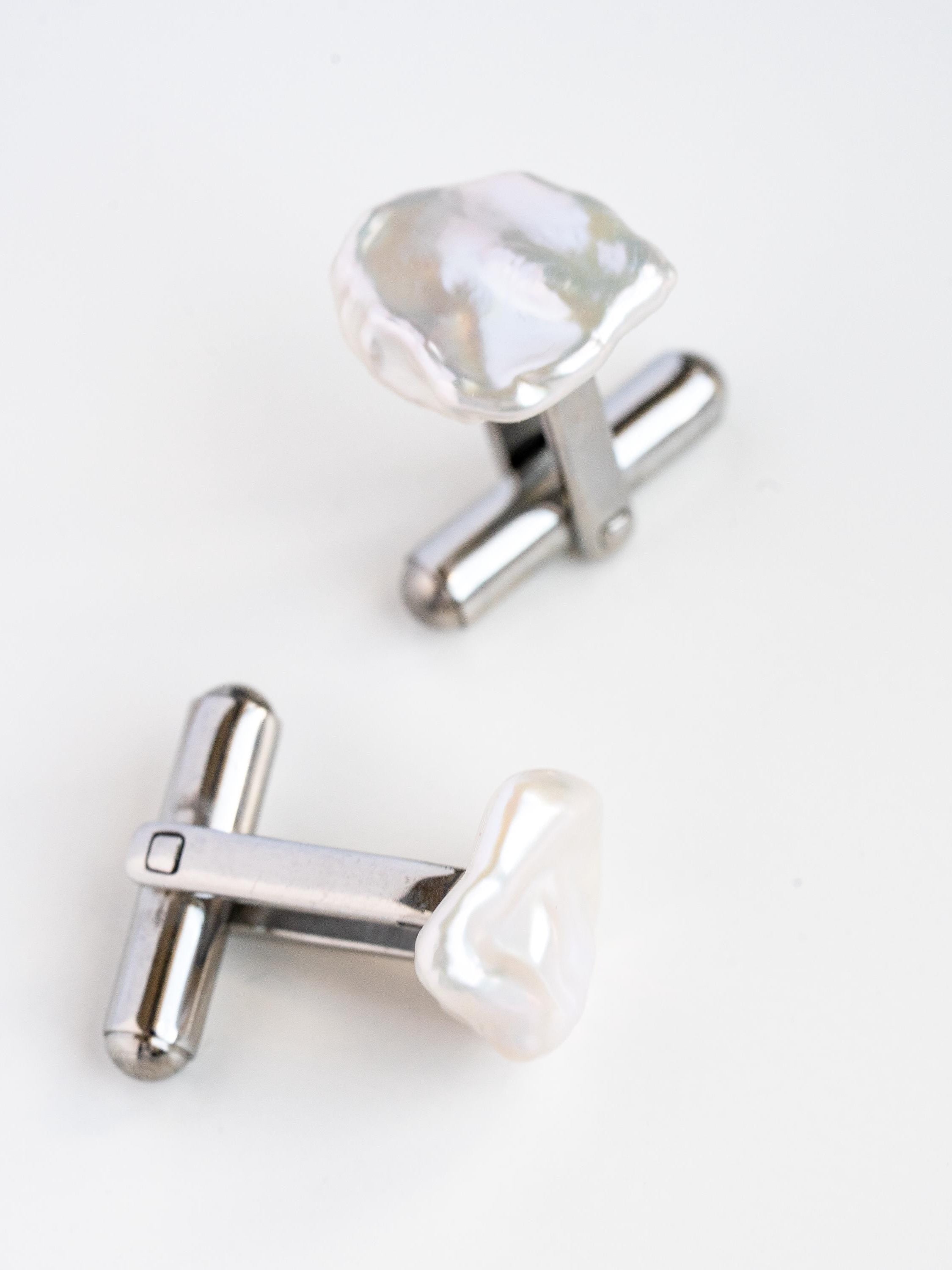 Silver cufflinks with heart-shaped pearls on a white background