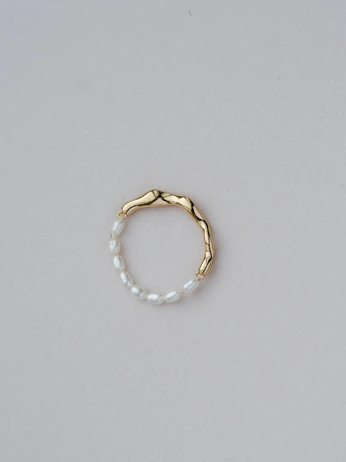 Gold ring with a white beaded band on a light gray background