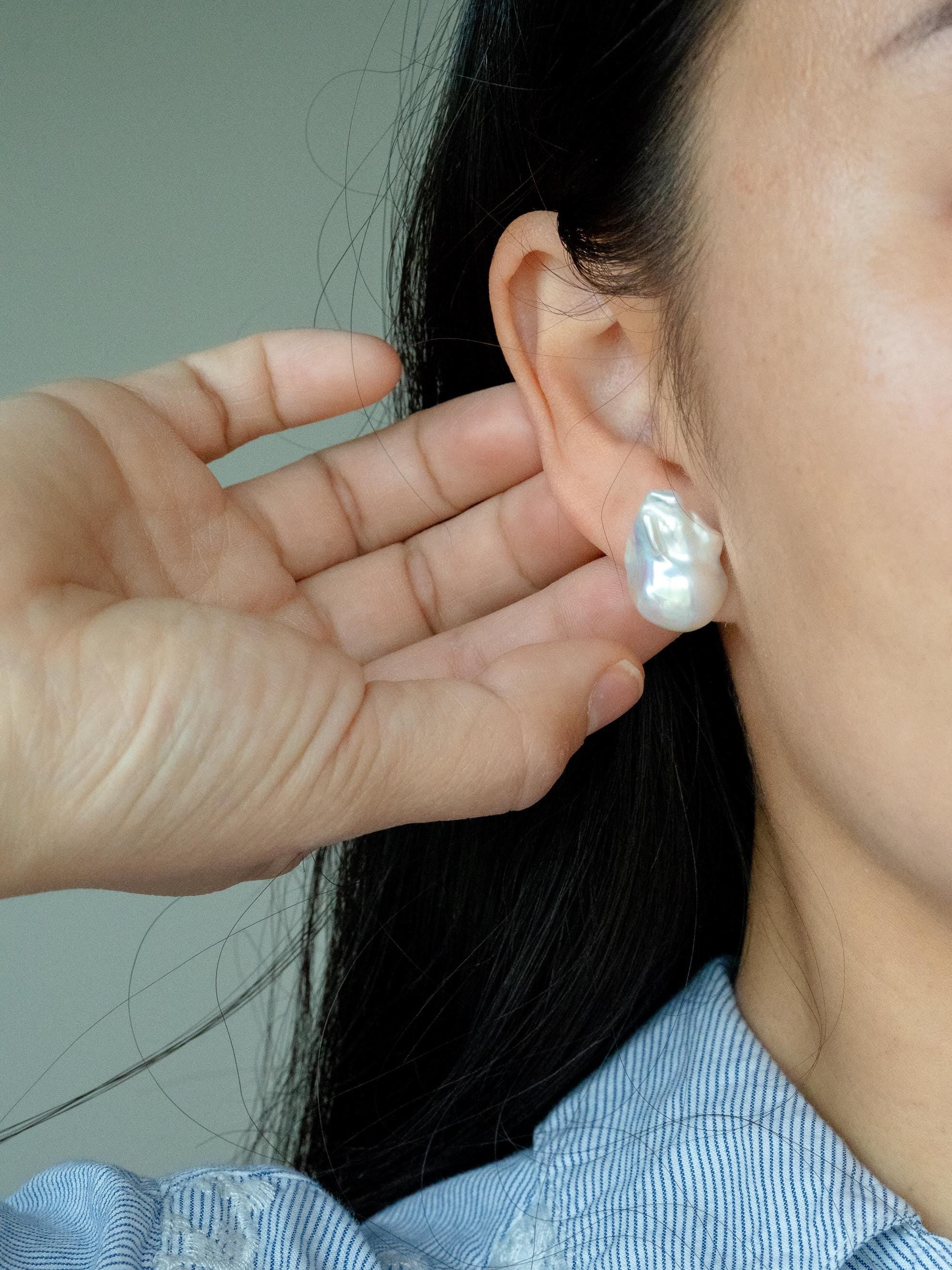 Person wearing a baroque pearl stud with a hand adjusting it against a neutral background