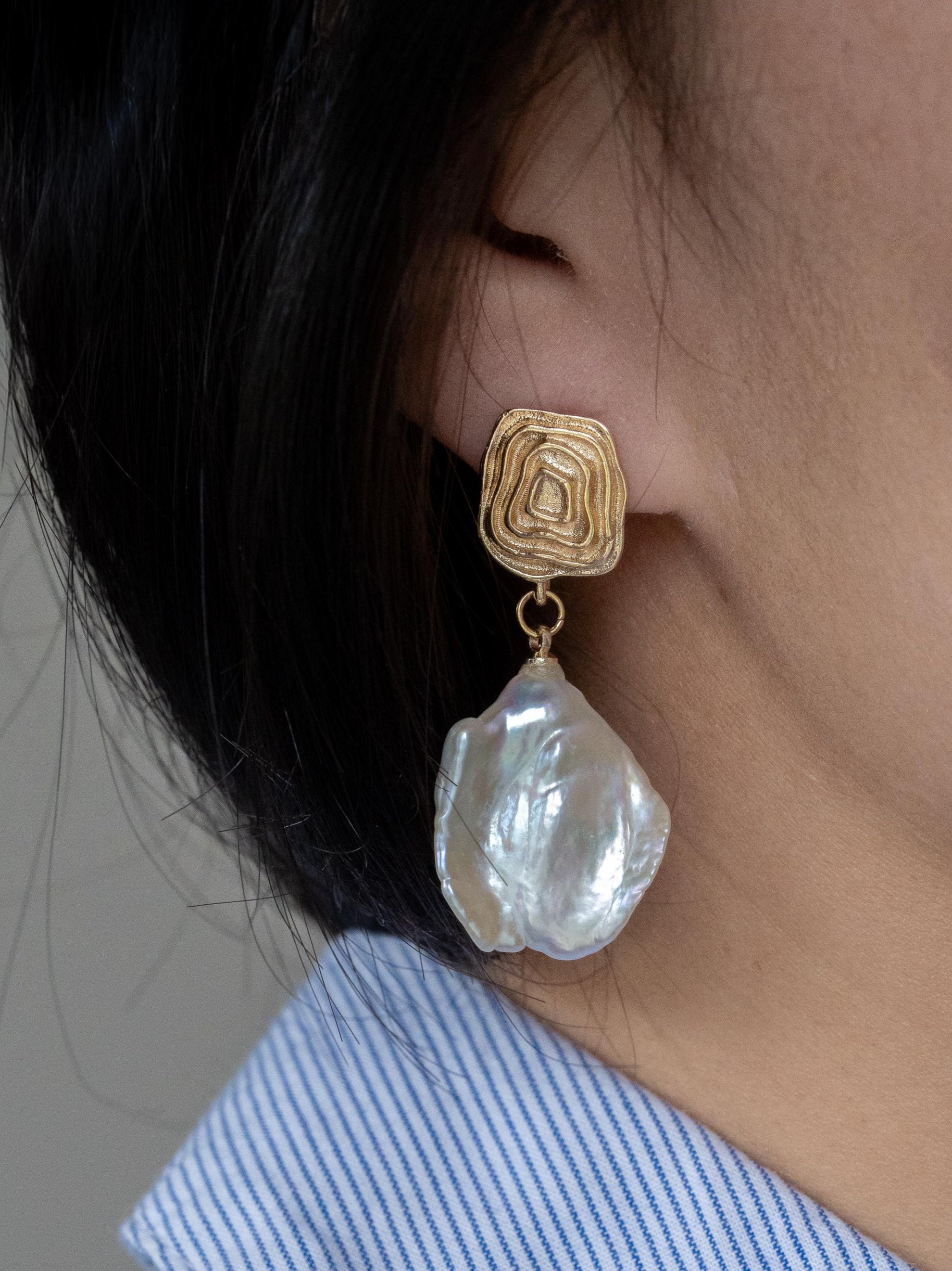 Close-up of a person wearing a gold earring with a large pearl